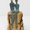 bronze sculpture on a travertine marble base by artist Yenny Cocq with two minimalist style figures in a green patina sitting atop the stone